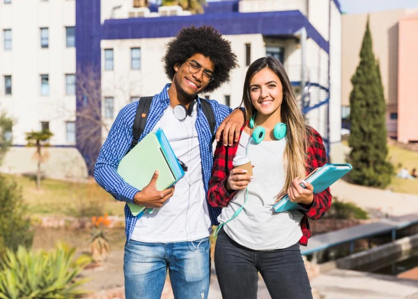 Estudantes jovens em um ambiente aberto, sendo um homem negro e uma mulher branca, ambos com material escolar nas mãos