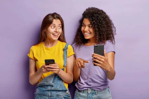 Duas mulheres com smartphones nas mãos com expressão de surpresa positiva