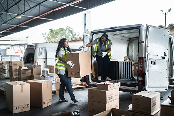 Duas mulheres carregando caixas e colocando em uma van